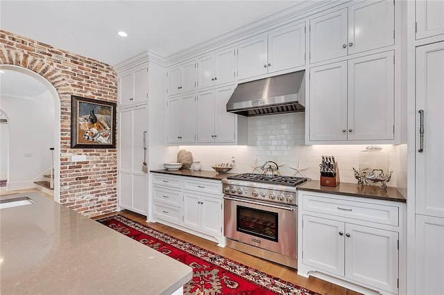 kitchen featuring stainless steel stove, light hardwood / wood-style flooring, extractor fan, decorative backsplash, and white cabinets