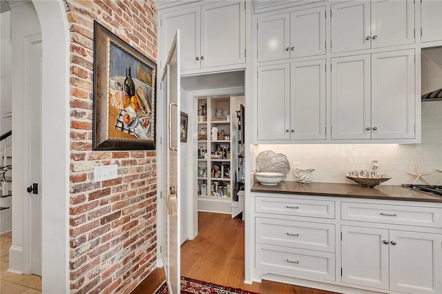 bar with white cabinets, backsplash, brick wall, and light hardwood / wood-style flooring