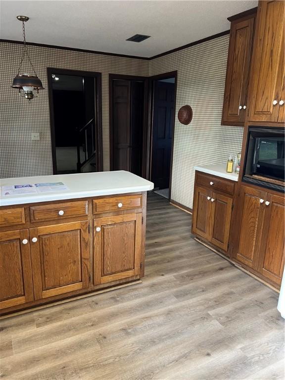 kitchen featuring pendant lighting, ornamental molding, black microwave, and light hardwood / wood-style flooring