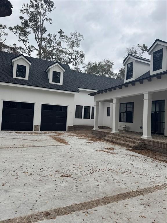 view of front of house with a shingled roof, concrete driveway, stucco siding, a porch, and a garage