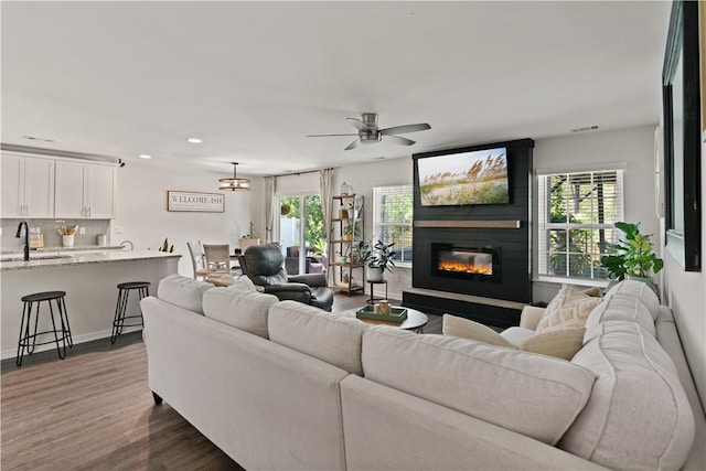 living room featuring ceiling fan, a large fireplace, a healthy amount of sunlight, and sink