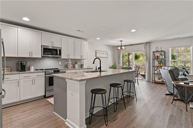 kitchen featuring stainless steel appliances, sink, pendant lighting, a center island with sink, and white cabinetry