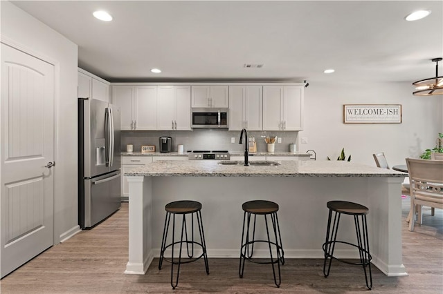 kitchen featuring sink, appliances with stainless steel finishes, a kitchen bar, white cabinets, and light wood-type flooring