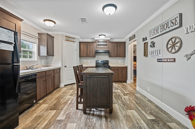 kitchen featuring dark brown cabinetry, sink, wood-type flooring, a kitchen island, and black appliances