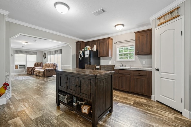 kitchen featuring black refrigerator, dark brown cabinetry, hardwood / wood-style flooring, and crown molding