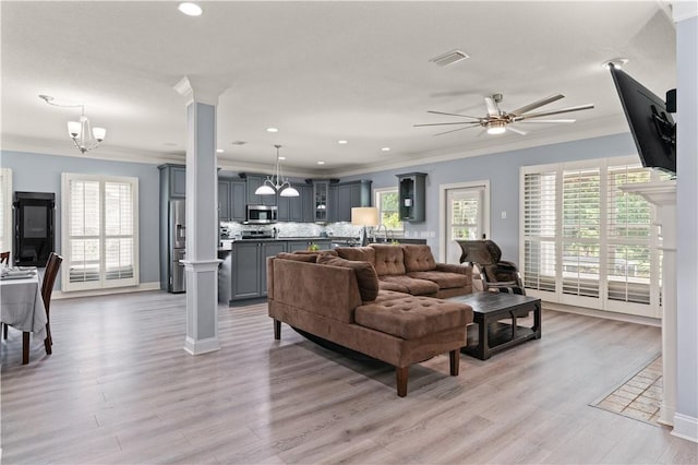 living room with decorative columns, light hardwood / wood-style floors, and ceiling fan with notable chandelier