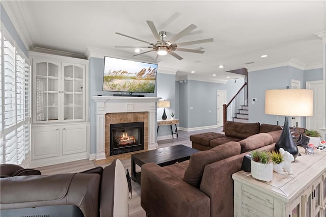 living room featuring light hardwood / wood-style flooring, ceiling fan, crown molding, and a tiled fireplace