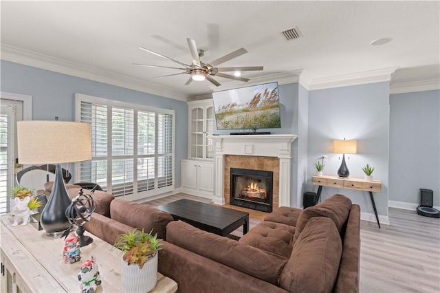 living room featuring a fireplace, light hardwood / wood-style flooring, ceiling fan, and crown molding