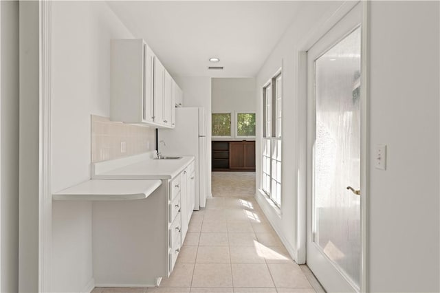 interior space featuring sink, light tile patterned floors, white fridge, decorative backsplash, and white cabinets