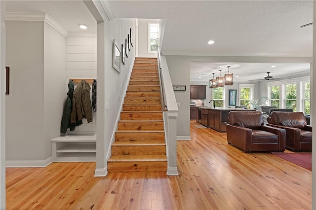 staircase featuring sink, crown molding, wood-type flooring, a textured ceiling, and ceiling fan with notable chandelier