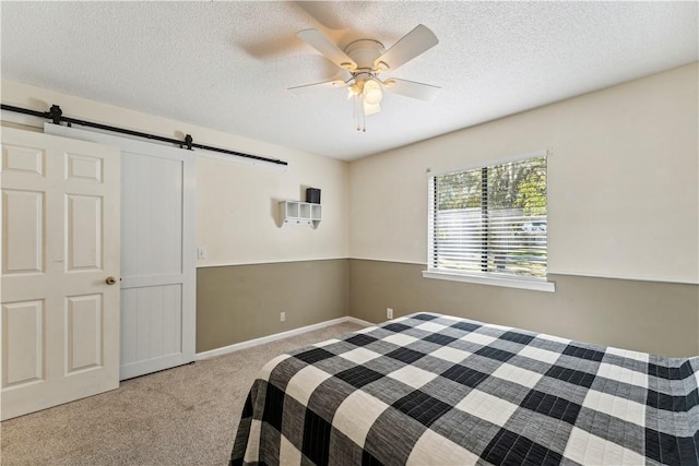 bedroom with a barn door, ceiling fan, light carpet, and a textured ceiling