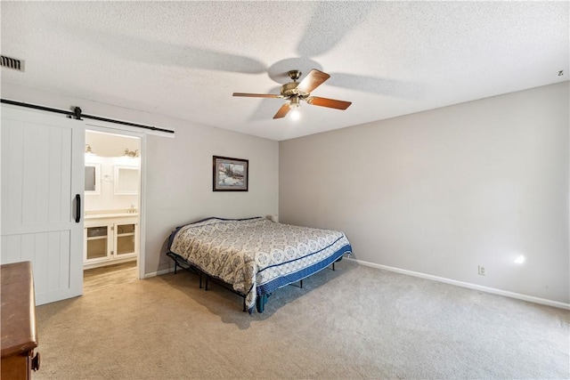 carpeted bedroom featuring a textured ceiling, a barn door, ensuite bath, and ceiling fan