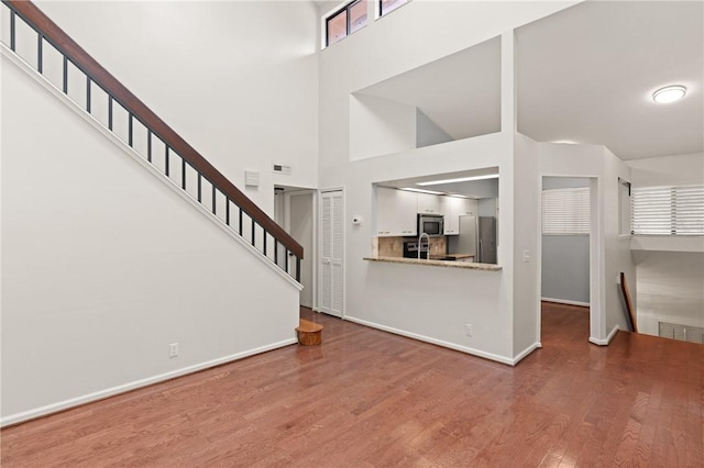893 Wimbledon Dr, Saint Simons Island, GA 31522 - unfurnished living room featuring wood finished floors, baseboards, a towering ceiling, and stairway
