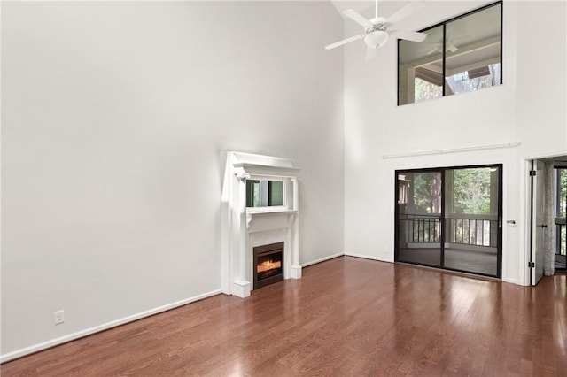 893 Wimbledon Dr, Saint Simons Island, GA 31522 - unfurnished living room with a high ceiling, a warm lit fireplace, a ceiling fan, wood finished floors, and baseboards