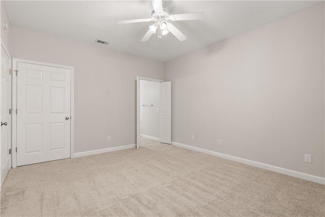 unfurnished bedroom featuring a ceiling fan, light colored carpet, visible vents, and baseboards