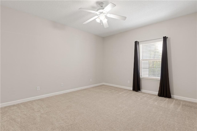 spare room with light carpet, a textured ceiling, baseboards, and a ceiling fan