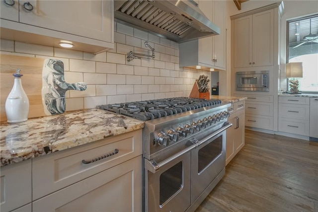 kitchen featuring light stone countertops, wall chimney exhaust hood, tasteful backsplash, light hardwood / wood-style floors, and appliances with stainless steel finishes