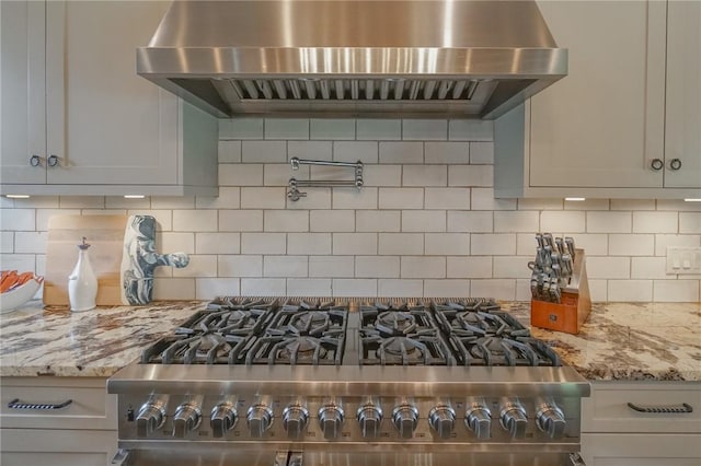 kitchen featuring tasteful backsplash, light stone counters, stainless steel range, and wall chimney exhaust hood