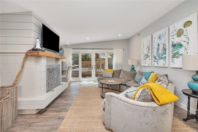 living room with a fireplace with raised hearth, recessed lighting, wood finished floors, vaulted ceiling, and french doors