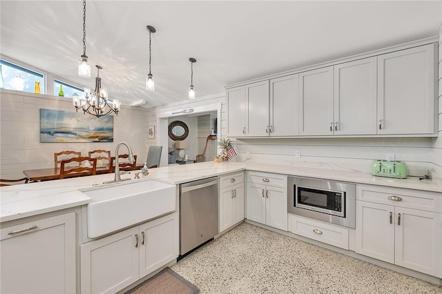 kitchen with hanging light fixtures, appliances with stainless steel finishes, light stone counters, and a sink