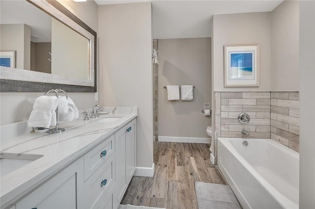 bathroom with a tub to relax in, toilet, wood finished floors, a sink, and baseboards