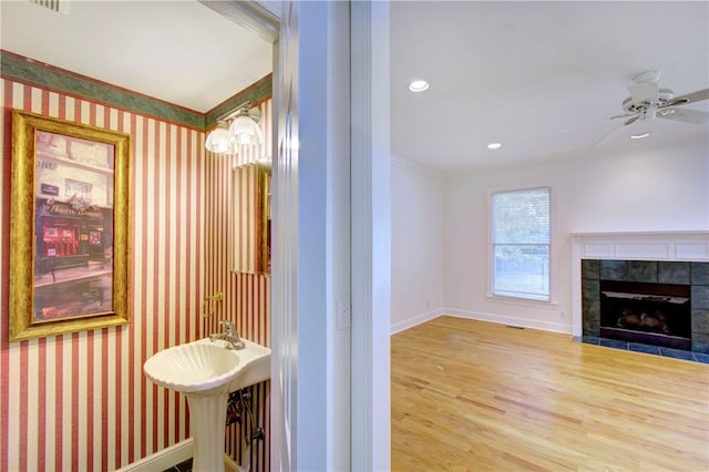 bathroom with hardwood / wood-style flooring, ceiling fan, and a tiled fireplace