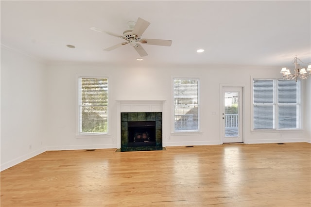 unfurnished living room featuring crown molding, a fireplace, ceiling fan with notable chandelier, and light hardwood / wood-style flooring