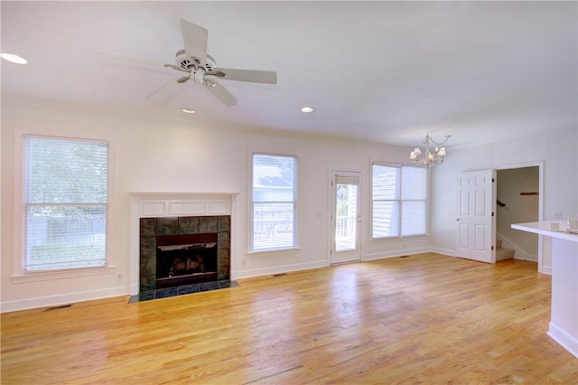 unfurnished living room with a tiled fireplace, ornamental molding, ceiling fan with notable chandelier, and light wood-type flooring