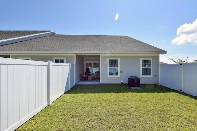 rear view of property with central AC unit, a lawn, a fenced backyard, and roof with shingles