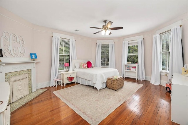 bedroom with visible vents, wood-type flooring, a premium fireplace, baseboards, and ceiling fan