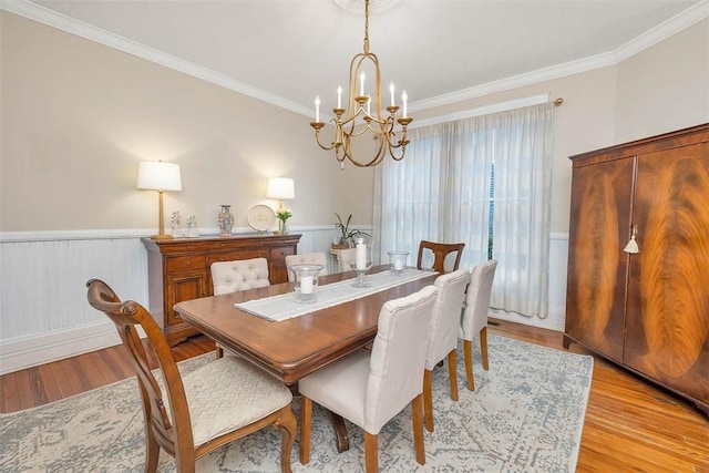 dining area featuring an inviting chandelier, crown molding, a wainscoted wall, and light wood-type flooring