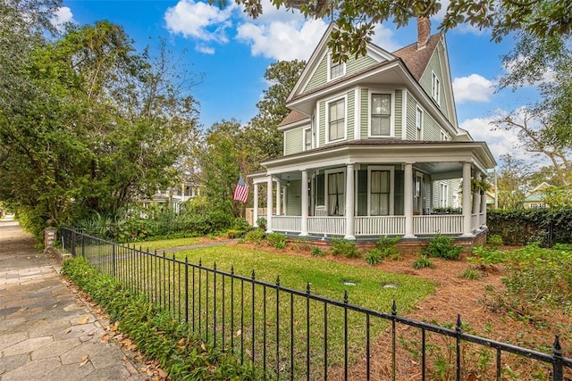 victorian house with a front lawn, a porch, a fenced front yard, and a chimney