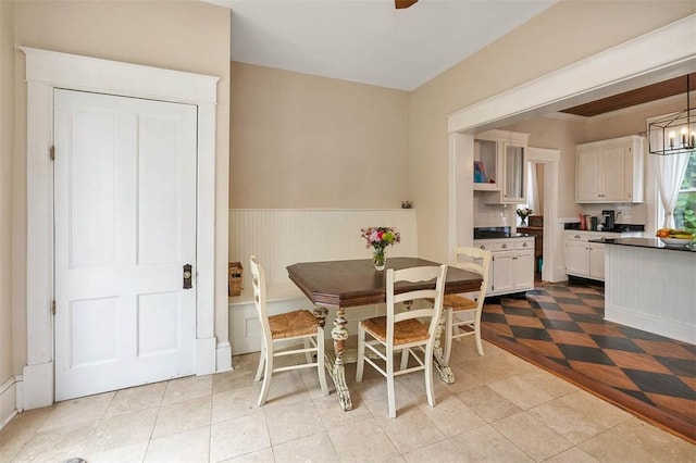 dining room with a wainscoted wall and ceiling fan with notable chandelier