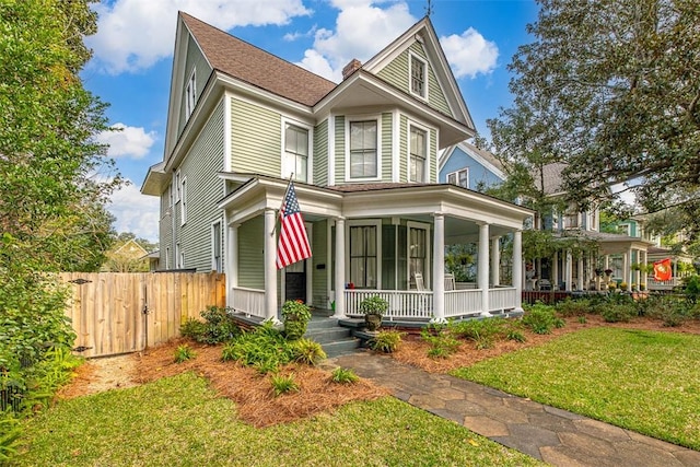 victorian home with a porch, a front lawn, and fence