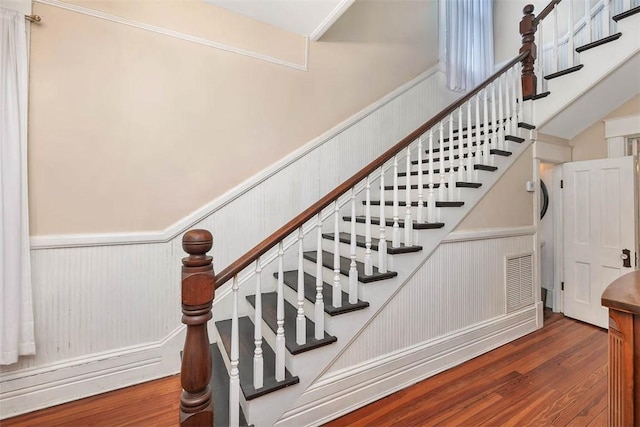 stairs with a high ceiling, wood finished floors, visible vents, and wainscoting