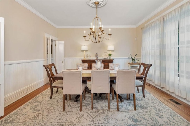 dining space with a chandelier, a wainscoted wall, crown molding, and wood finished floors