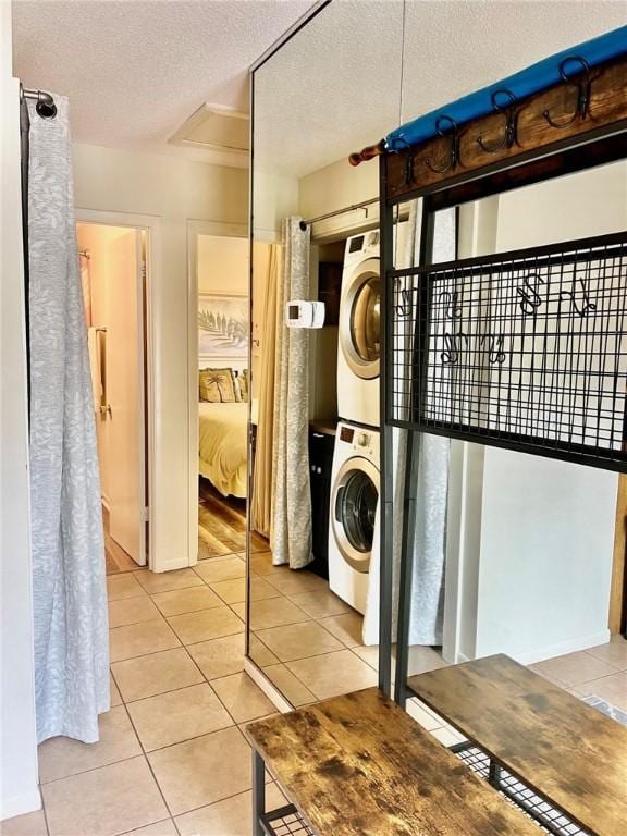 laundry area with a textured ceiling, light tile patterned floors, and stacked washer / dryer