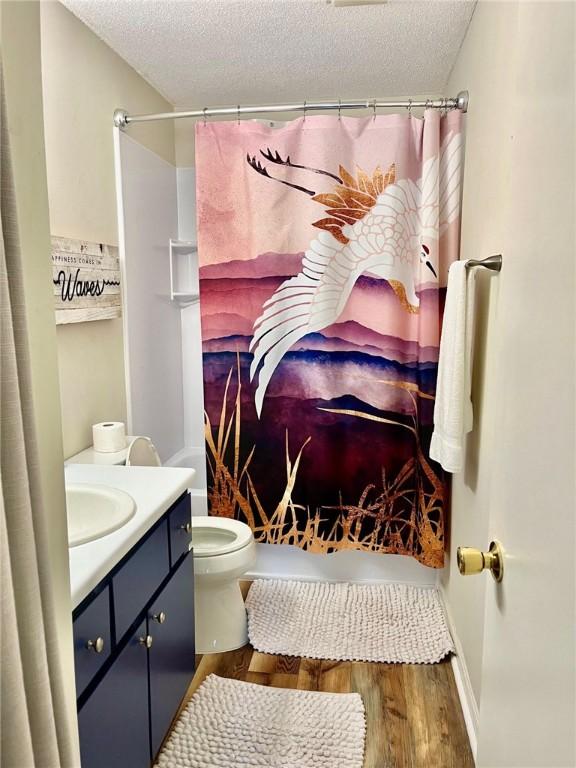 full bathroom featuring vanity, a textured ceiling, shower / tub combo with curtain, wood-type flooring, and toilet