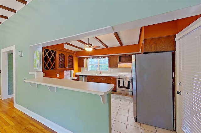 kitchen with stainless steel appliances, a kitchen bar, a sink, a peninsula, and light countertops