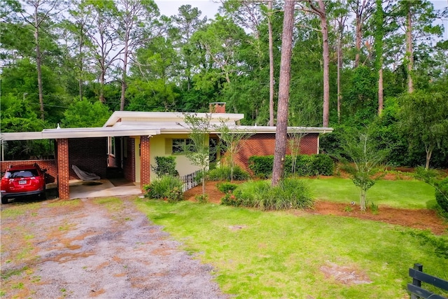 view of front of house featuring dirt driveway, a front yard, brick siding, a chimney, and an attached carport