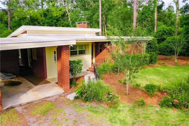 view of front of home with a chimney, brick siding, an attached carport, and a front yard