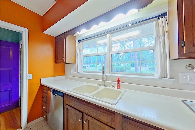 kitchen featuring stainless steel dishwasher, a sink, brown cabinets, and light countertops