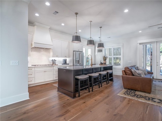 kitchen featuring appliances with stainless steel finishes, a kitchen island with sink, dark hardwood / wood-style flooring, custom range hood, and white cabinets