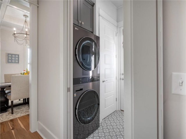 laundry area with hardwood / wood-style floors, crown molding, an inviting chandelier, stacked washing maching and dryer, and cabinets