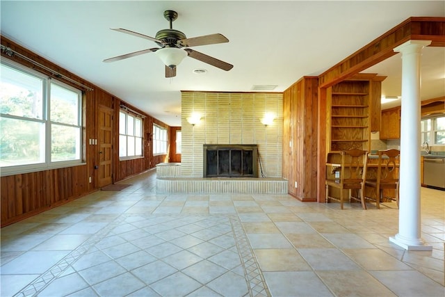 unfurnished living room with decorative columns, ceiling fan, wooden walls, a fireplace, and light tile patterned flooring