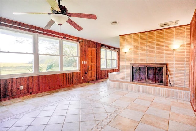 unfurnished living room with wood walls, ceiling fan, light tile patterned floors, and a brick fireplace