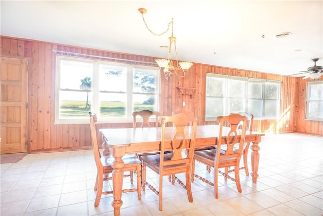 dining space featuring wooden walls, ceiling fan with notable chandelier, light tile patterned floors, and a wealth of natural light