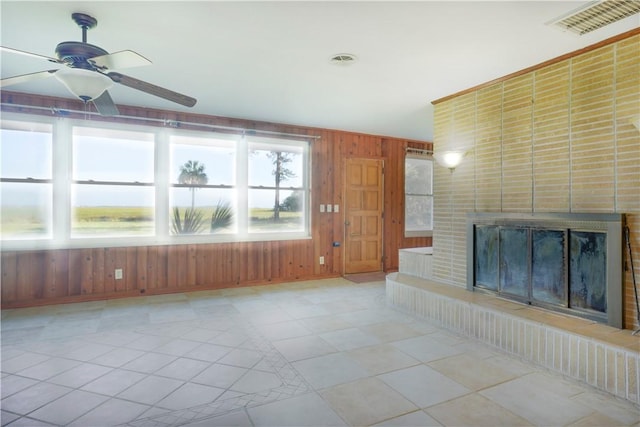 unfurnished living room featuring wooden walls, a fireplace, ceiling fan, and light tile patterned flooring