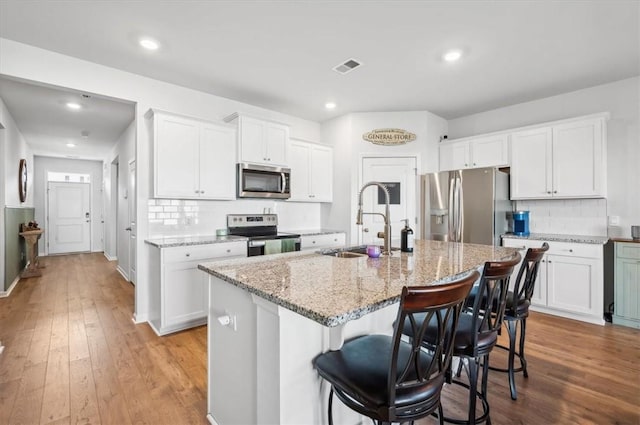 kitchen featuring appliances with stainless steel finishes, light wood-type flooring, sink, a center island with sink, and white cabinets