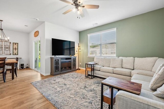 living room featuring ceiling fan with notable chandelier and light wood-type flooring